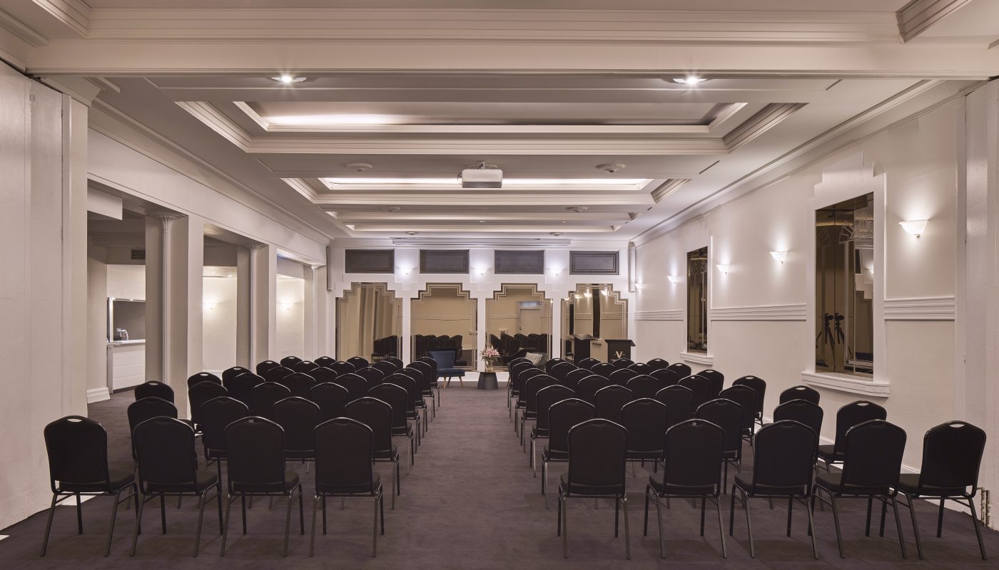 Rows of black chairs line a bright conference room, with a central aisle leading toward the front.